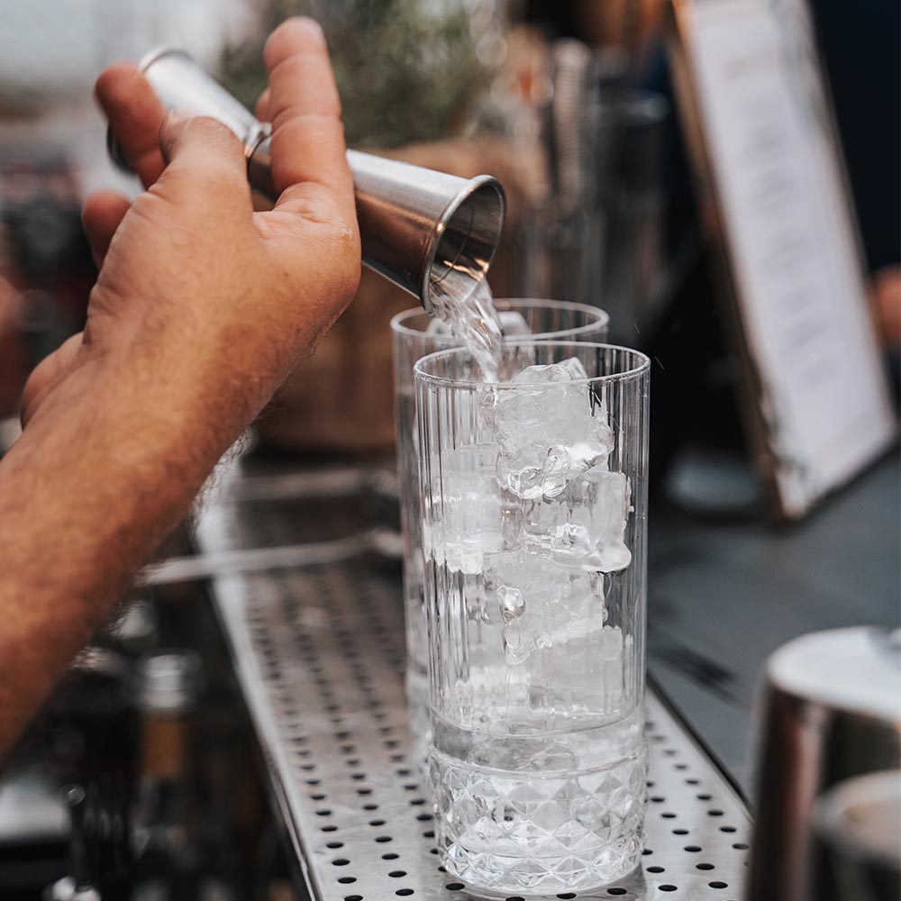 Mano che versa drink nei bicchieri pieni di ghiaccio